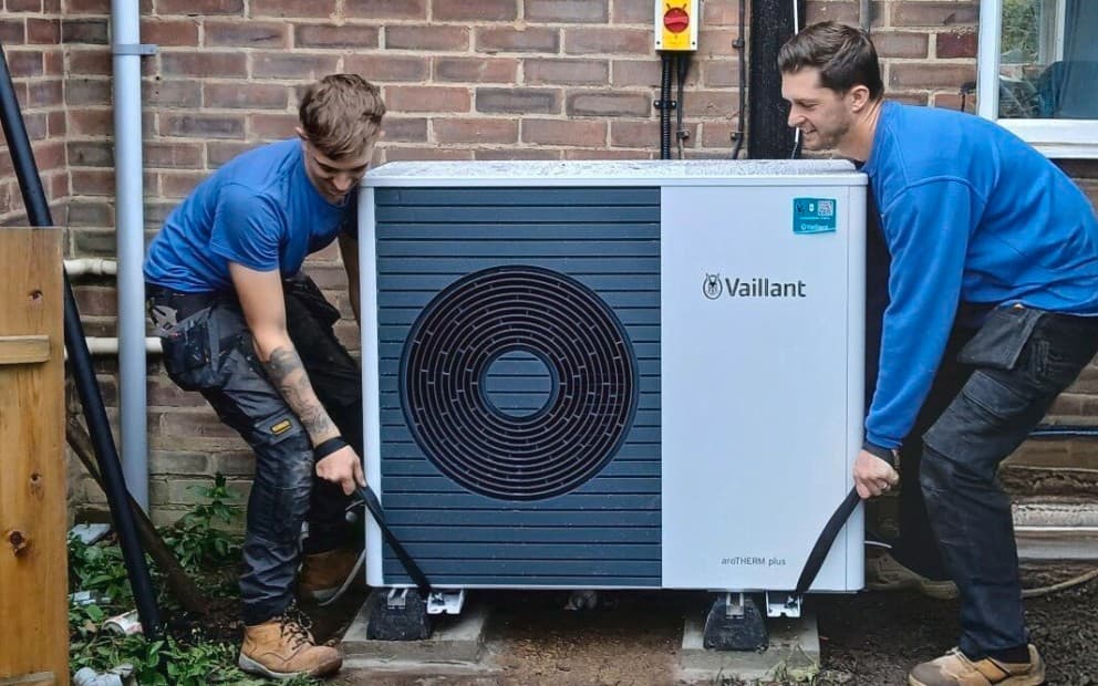 Two installers holding straps lowering a Vaillant aroTHERM plus heat pump to the ground.