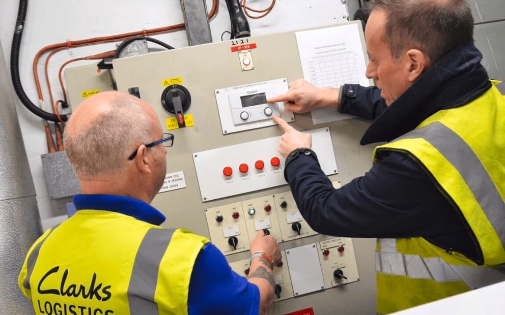 Two men in yellow vests examining a machine interface.