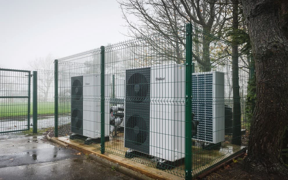 Two heat pump units behind a green casing.