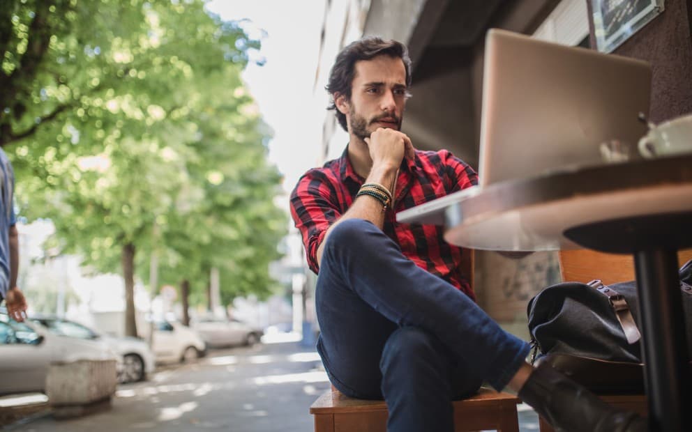 Man sat outside at a table looking at an open laptop.