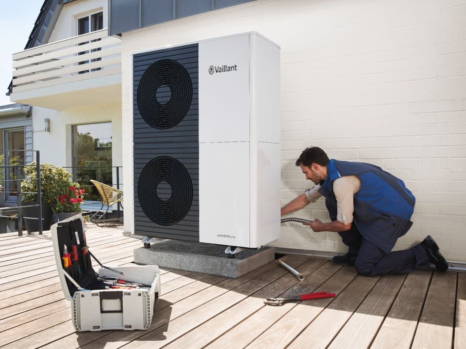 A man is installing a heat pump, focused on the equipment with tools in hand.