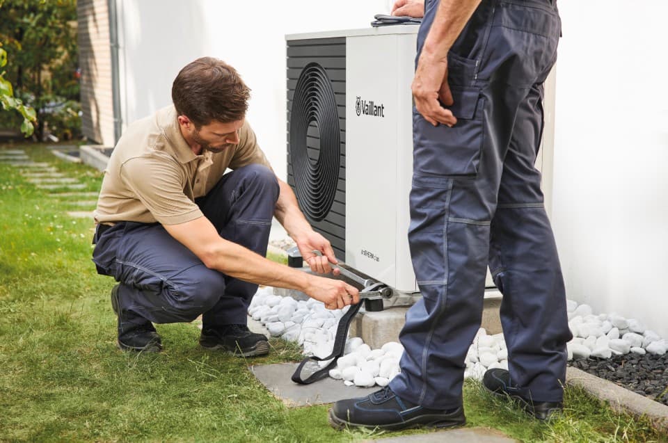 A installer kneeling down holding a spanner carrying out work on a heat pump.