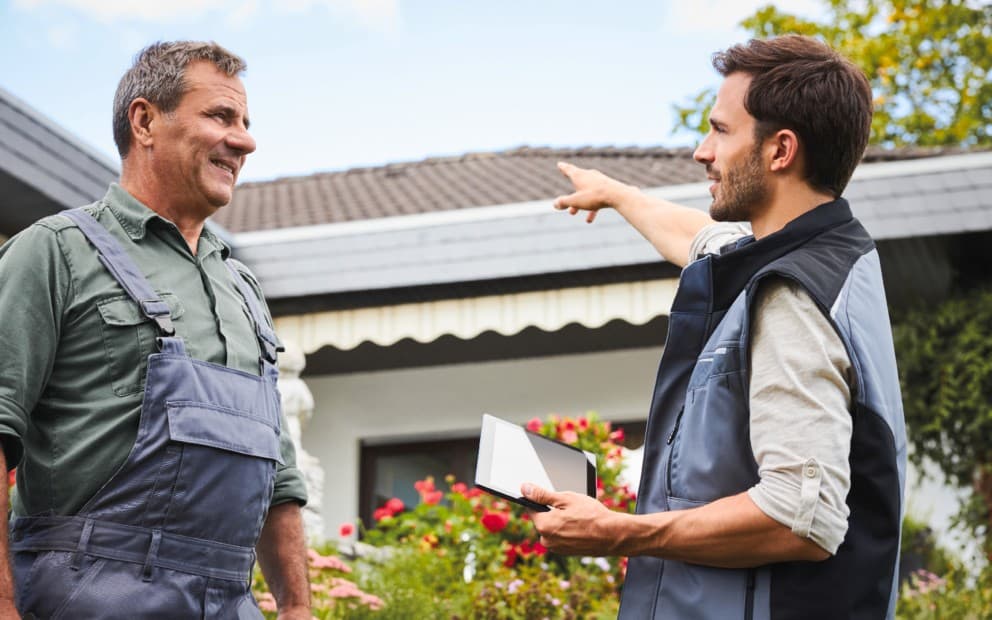 Two installers talking, one is pointing at a roof whilst holding a tablet.