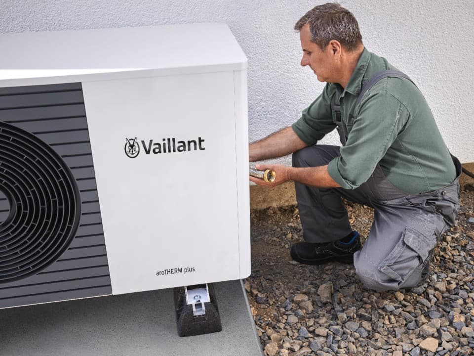 Man kneeling down doing work at the back of a heat pump unit