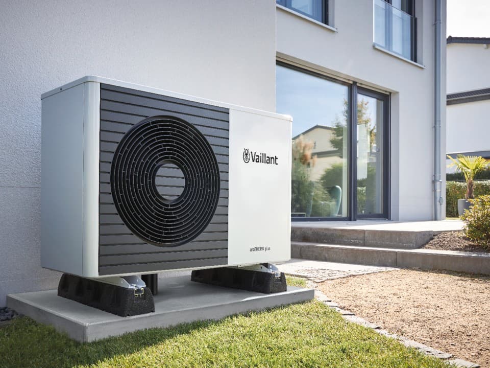 Heat pump unit outside a large white house with windows.