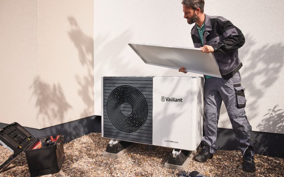 An installer holding a white metal sheet to put on top of a heat pump.
