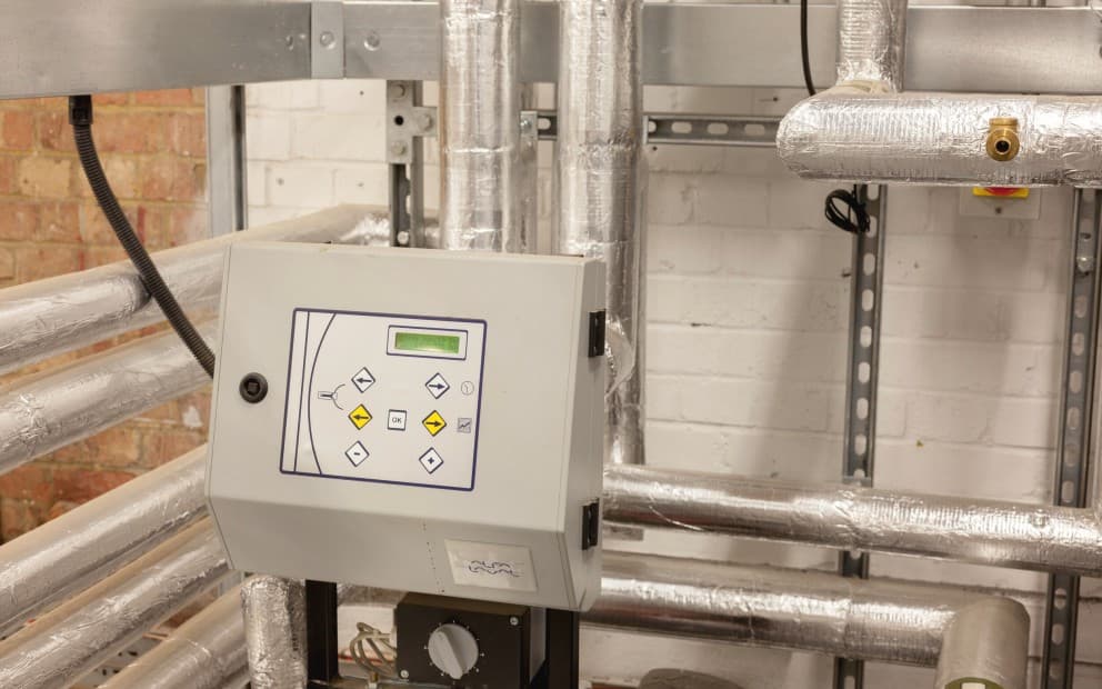 A control panel displayed in a room filled with various pipes and industrial equipment.