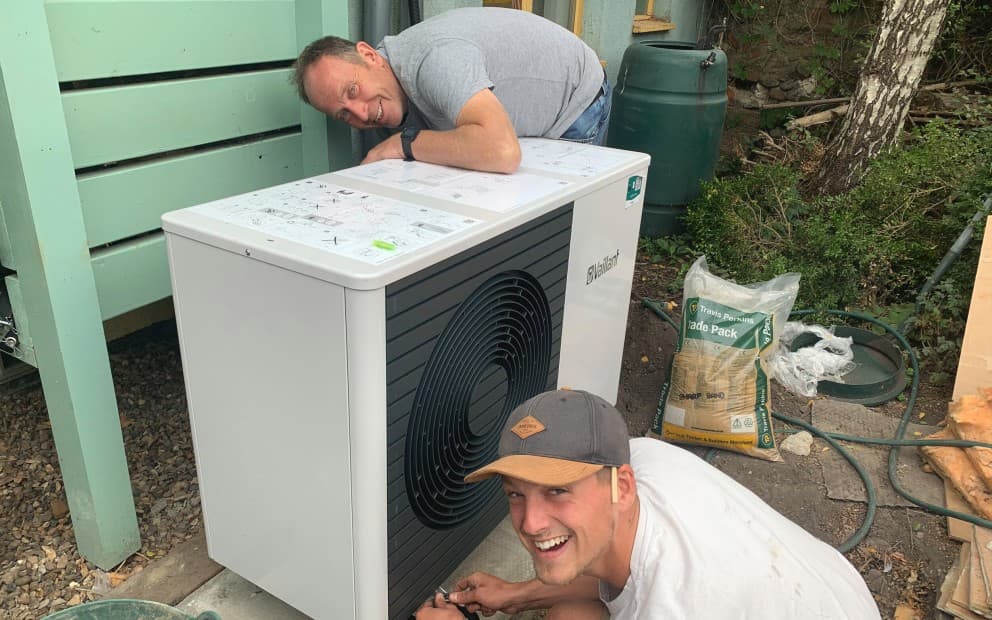 Two men doing work on a heat pump unit