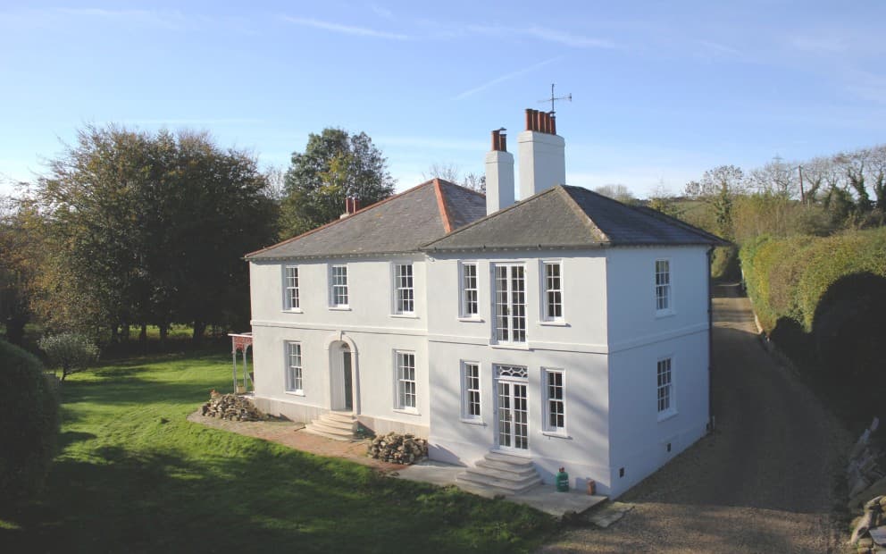 A large white house surrounded by a spacious green lawn under a clear blue sky
