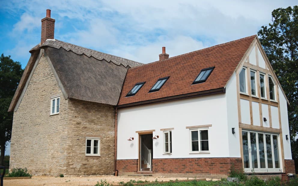 A quaint house featuring a thatched roof and multiple windows, set against a natural backdrop.