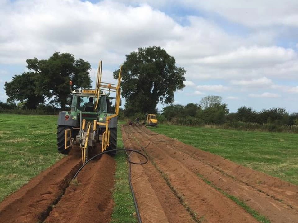 A tractor in a field installing underground pipes into the soil.