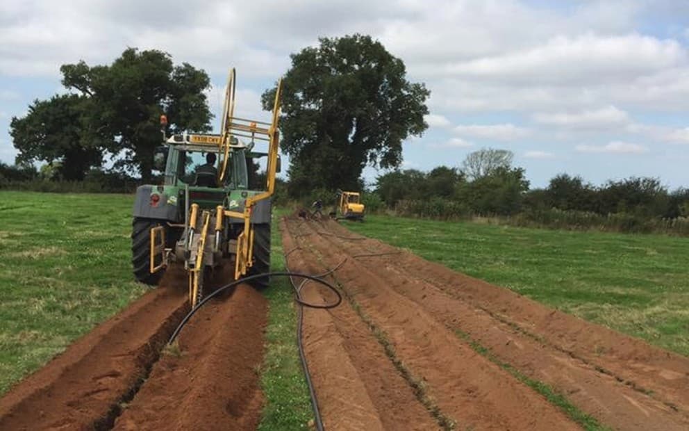 A tractor in a field installing underground pipes into the soil.