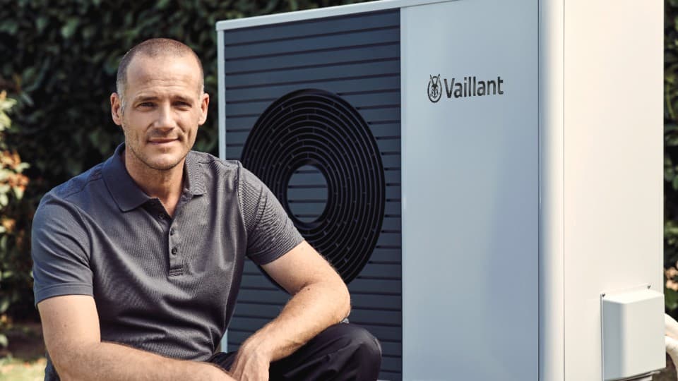 A man facing forwards with a Vaillant heat pump in the background.