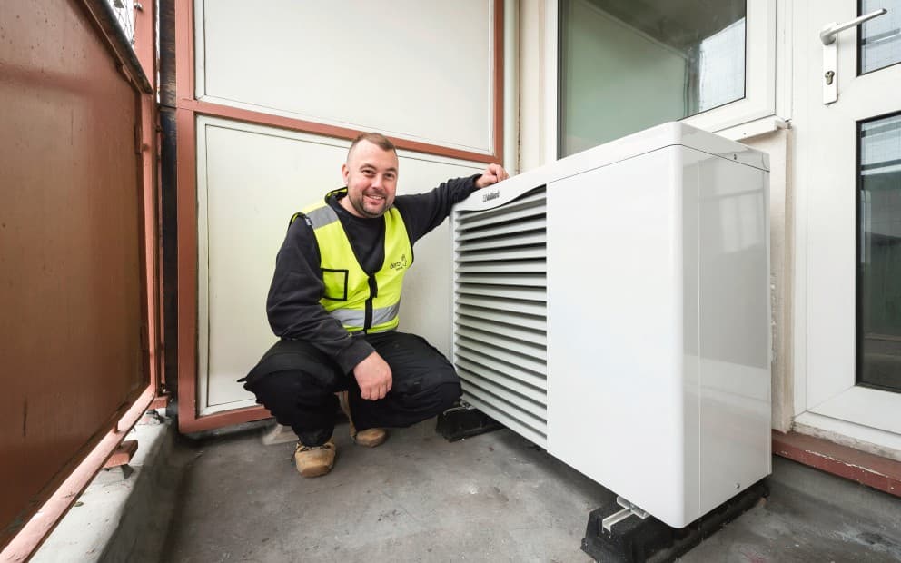 Man kneeling down with his arm on top of the heat pump unit