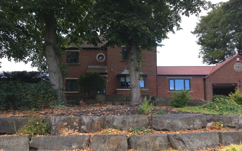 A house with a stone wall and trees in front, showcasing a serene outdoor setting.