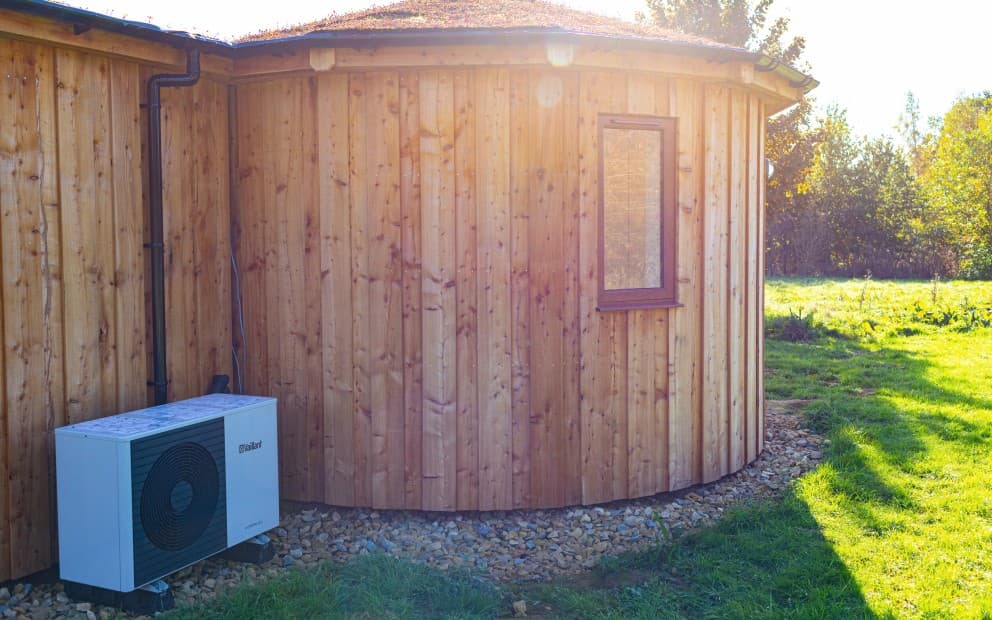 A small wooden house featuring a Vaillant air source heat pump unit on the left side.