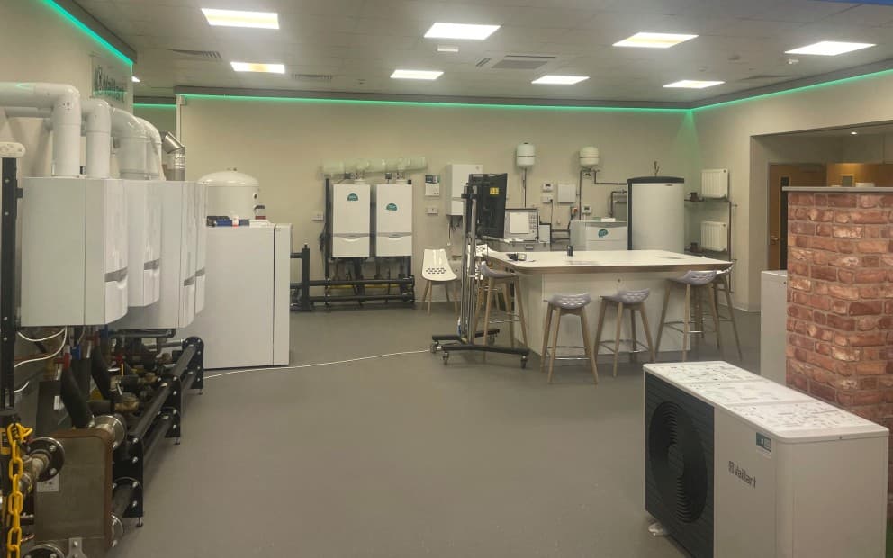 A room filled with various equipment, including boilers, heat pumps, a desk, and chairs.