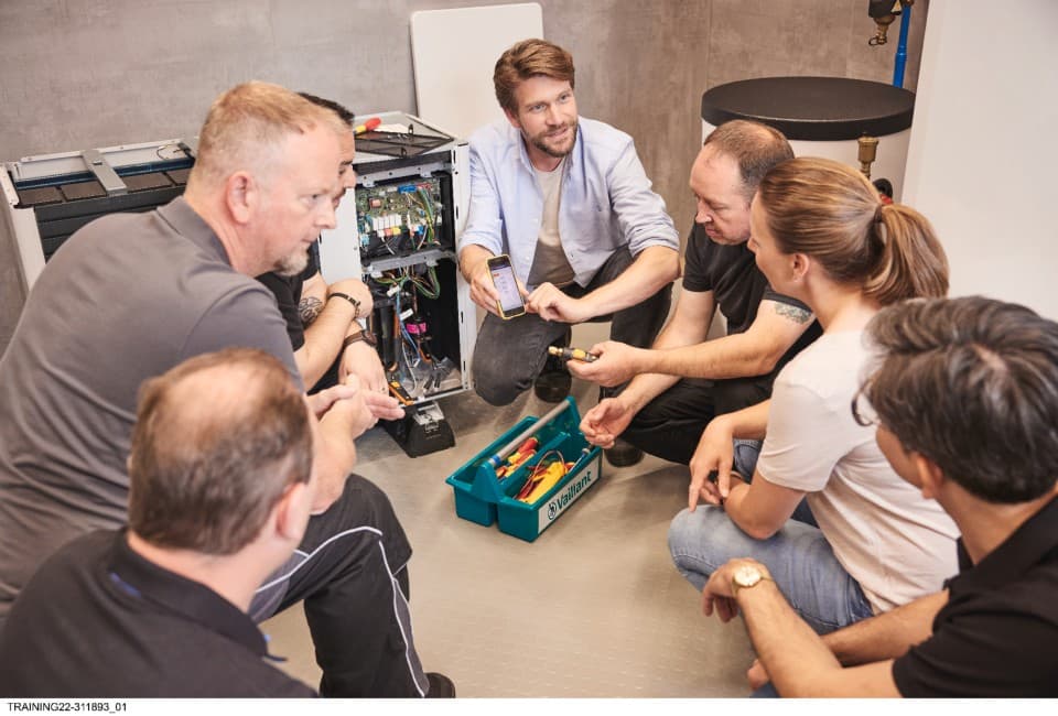 A group of people kneeling down looking at the insides of a heat pump on a training session.