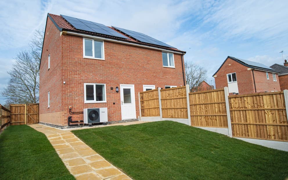 Brick house with wooden fencing, grass and a heat pump. There are solar panels on the roof.