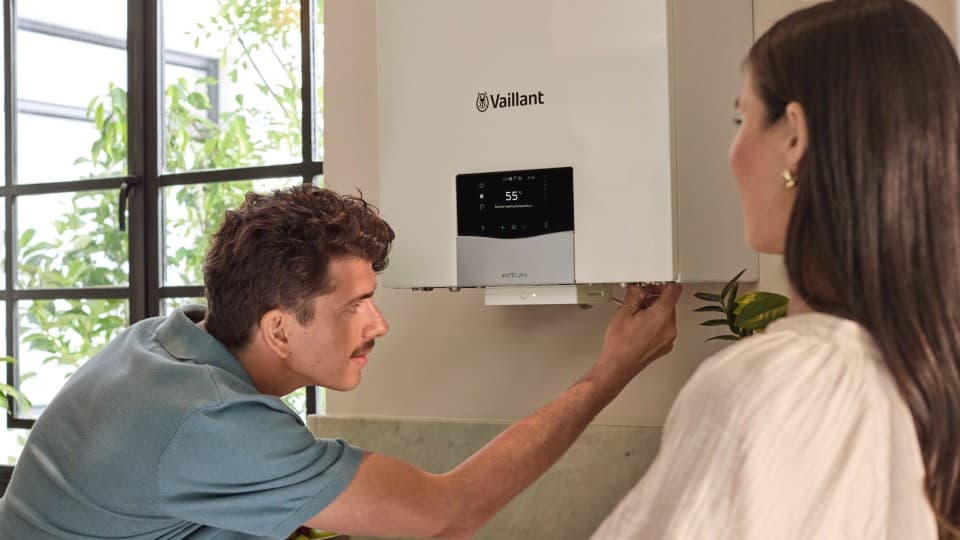 man looking at the underneath of a boiler with a woman watching him work.