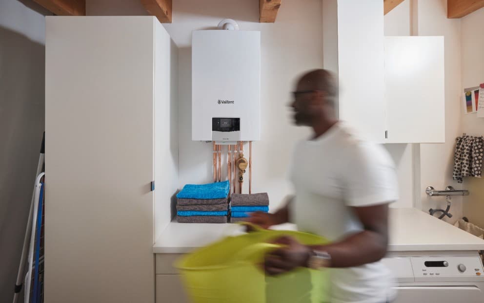 Man carrying a washing basket walking through a utility room with a ecoTEC plus boiler in the background