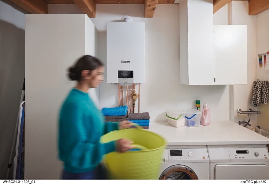 A woman carrying a laundry basket through a utility room. There is a boiler on the wall in the background.