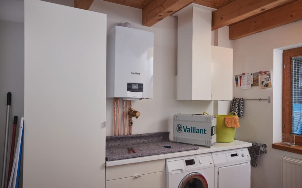 A side view of a boiler on the wall. There is a briefcase on the worktop with the Vaillant logo.