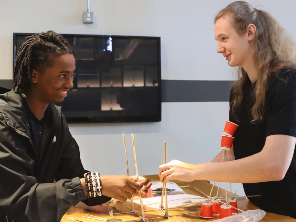 Two students building a sculpture out of paper and straws.